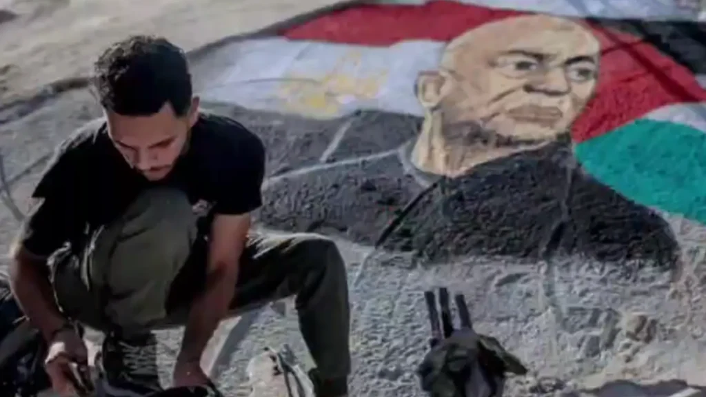 Gambar foto realistik seorang artis Palestin sedang melukis potret jurulatih Mesir Hossam Hassan di atas runtuhan bangunan Gaza
